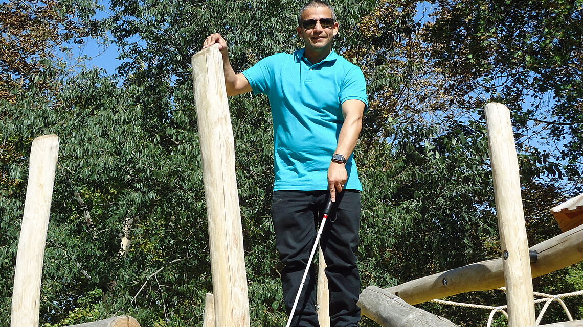 Juan Ruiz mit Weißem Stock am Klettergerüst eines Spielplatzes