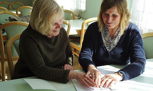 Die beiden Damen ertasten lachend die Inhalte einer Broschüre in Braille Schrift