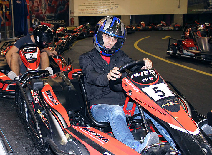 Ein Jugendlicher mit Helm sitzt im vordersten Go Kart, hat die Hände fest am Lenkrad und blickt startbereit in die Kamera. Dahinter richtet sich ein weiterer Jugendlicher gerade im Kart ein.