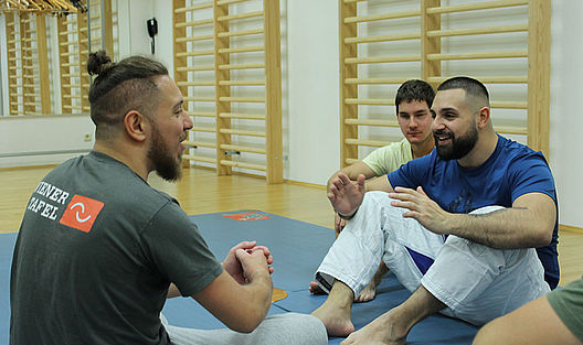 Im lockeren Gespräch nach dem Training sitzen die Teilnehmer auf den blauen Matten zusammen. 