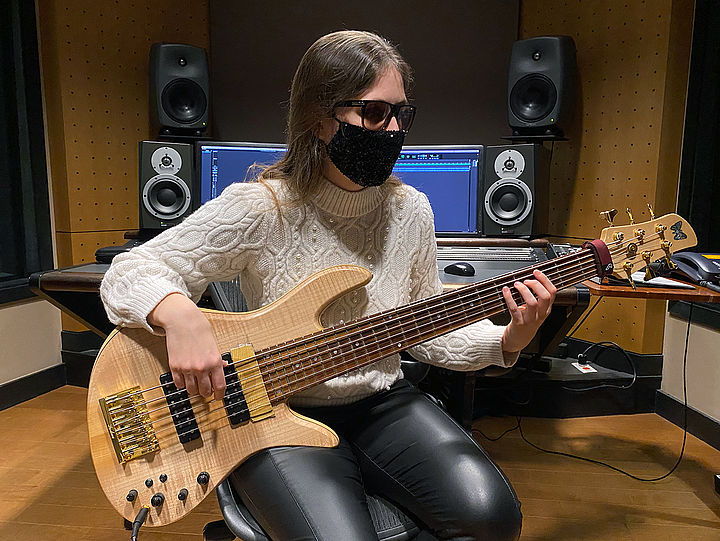 Ciara mit Mundschutz am Bass, hinter ihr sieht man Studioequipment wie Boxen und Monitore.
