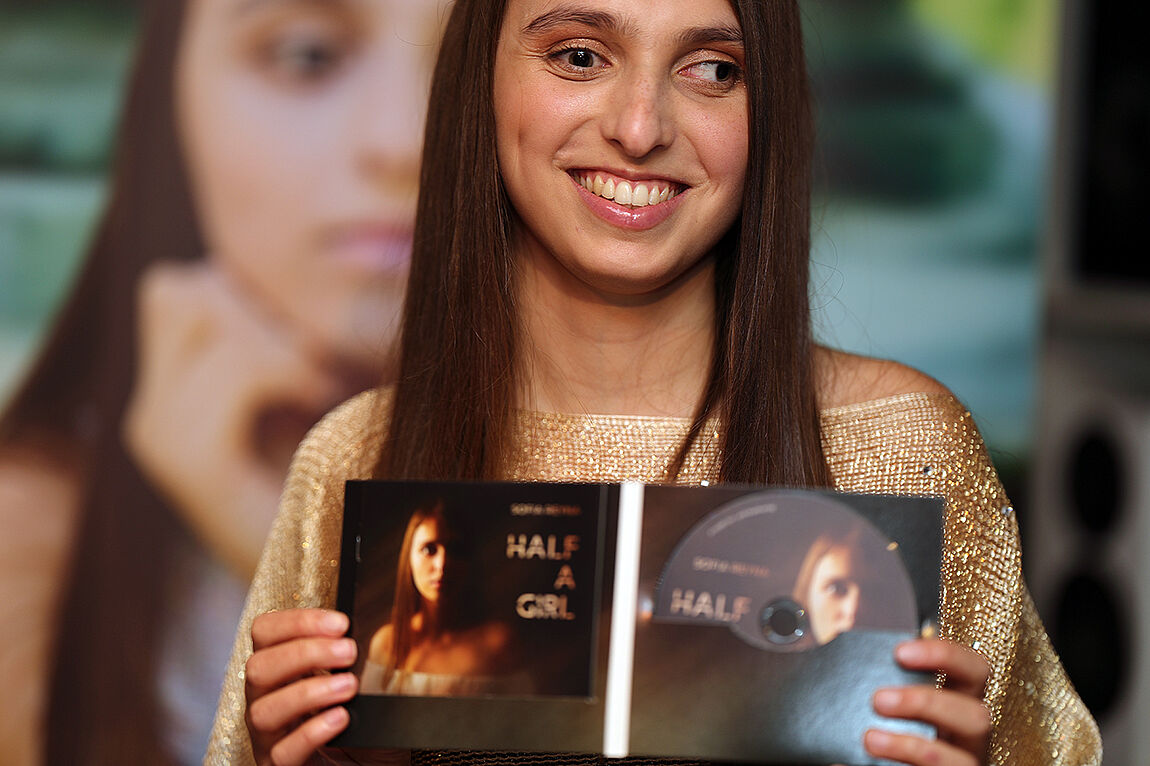 Eine lachende junge Frau zeigt das aufgeklappte CD-Album in die Kamera. 