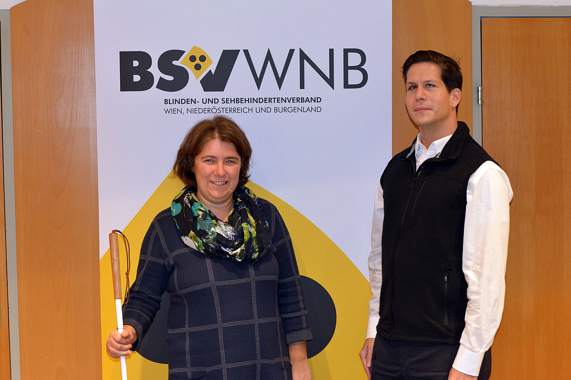 Marion Putzer-Schimack und Mag. Aaron Banovic stehen vor dem BSVWNB-Logo in den Louis Braille Stuben