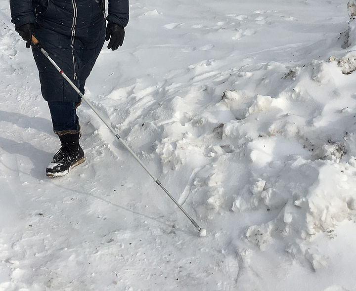Jemand ertastet mit dem weißen Stock einen Weg durch hohen Schnee.