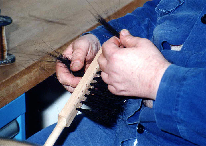 Nahaufnahme zweier Hände, die Borsten in einen Bürstenkopf einziehen