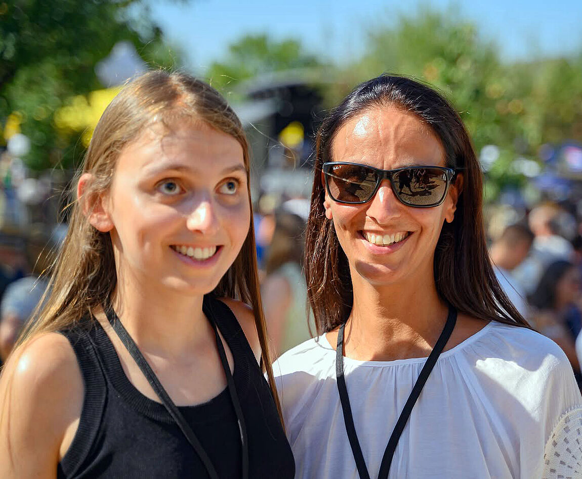 Zwei lachende Frauen bei einer Open-Air-Veranstaltung, die Mutter trägt eine Sonnenbrille.