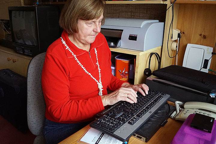 Eva am Bürosessel, vor sich eine Computer-Tastatur mit zusätzlicher elektronischer Braillezeile.
