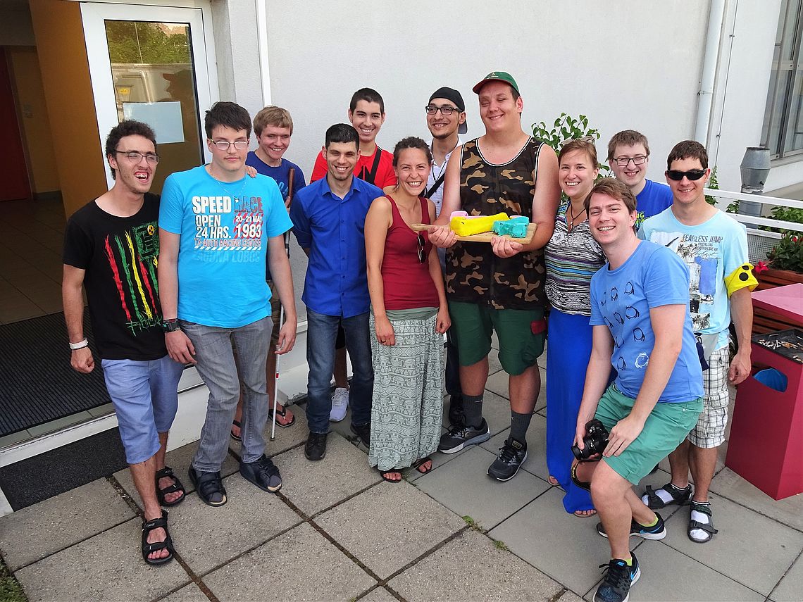 Auf einer Dachterrasse stehen die beiden Projektleiterinnen inmitten von 10 Jugendlichen, einer hält eine Geburtstagstorte; alle lachen in die Kamera