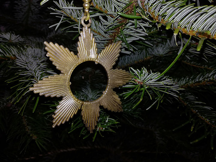 Nahaufnahme eines güldenen Plastiksterns inmitten von Zweigen einer Tanne.