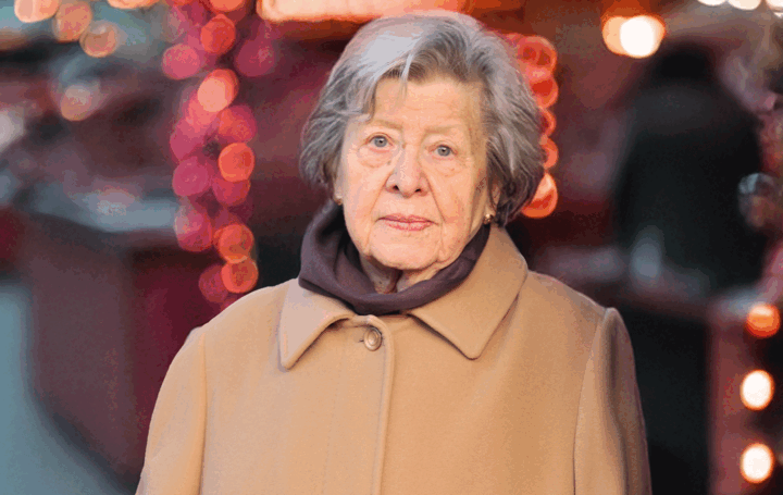 Eine ältere Dame im Wintermantel. Im Hintergrund ist schemenhaft ein Weihnachtsmarkt erkennbar.