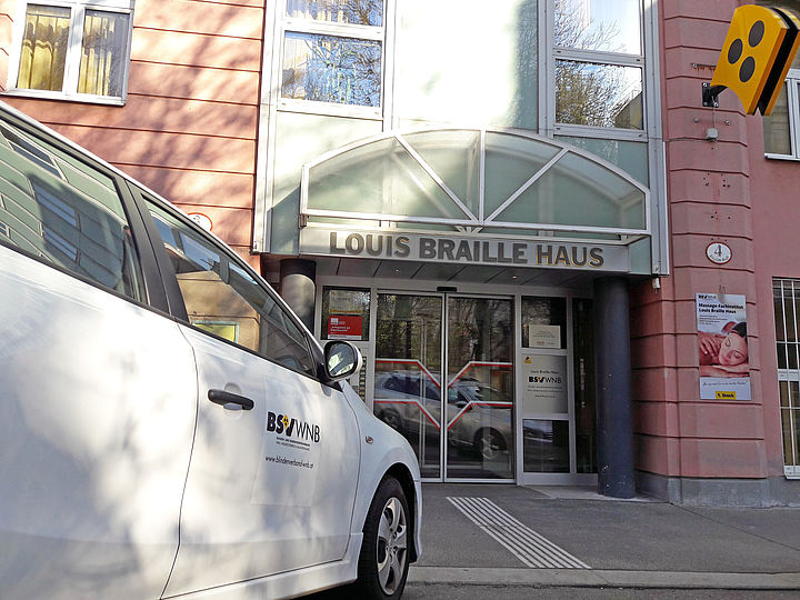 Vor dem Haupteingang des Louis Braille Hauses mit geschlossenen Schiebetüren ist das Dienstauto einer Sozialberaterin abgestellt.