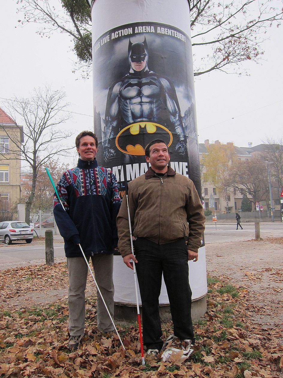 Die "Fledermausmänner" Daniel Kish und Juan Ruiz vor einer Litfaßsäule mit einem "Batman"-Plakat