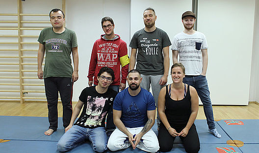 Die Gruppe von sieben KampfsportlerInnen steht oder kniet für ein Gruppenfoto auf der Matte.