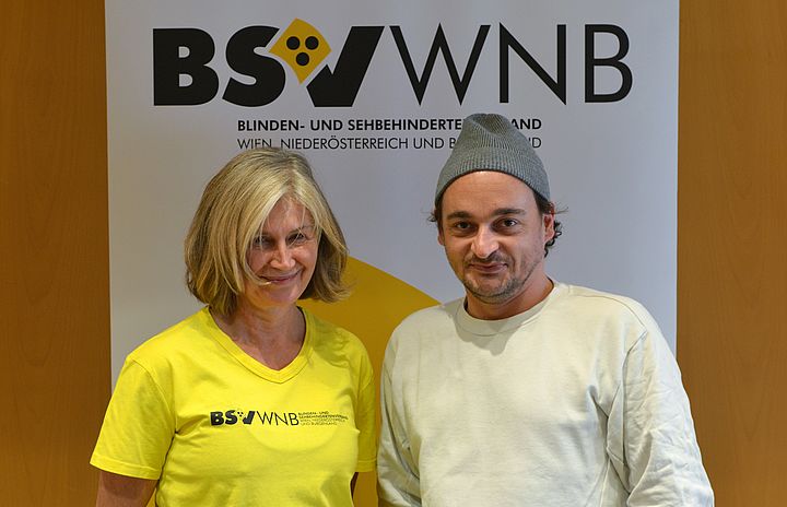 Die Trainerin und der Schauspieler lachen vor dem BSVWNB-Logo stehend verschmitzt in die Kamera
