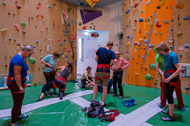 In einer Kletterhalle legen ein halbes Dutzend Menschen Klettergeschirr an.