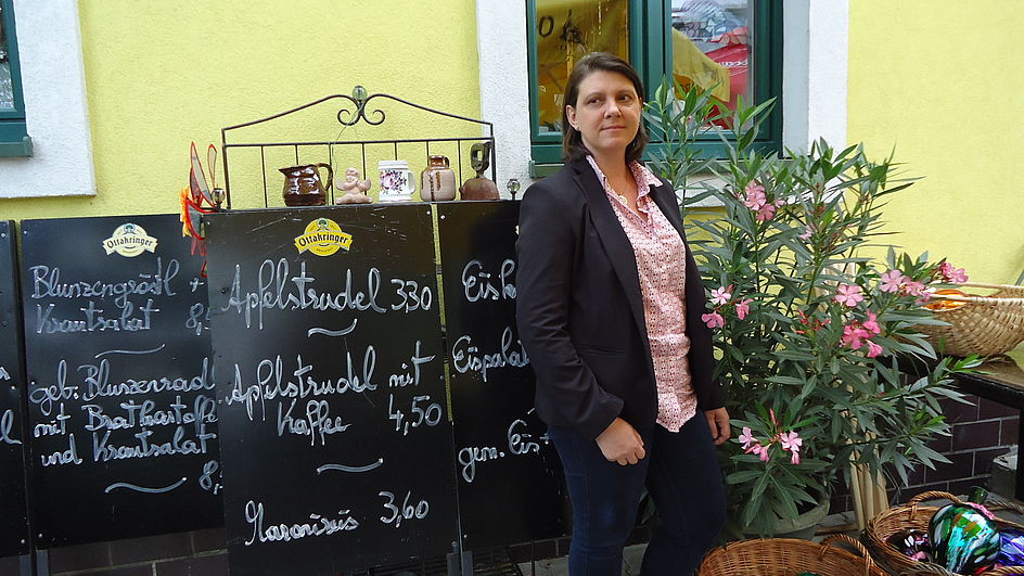 Barbara Probst steht selbstbewusst neben den Aufstellern mit gastronomischen Schmankerln, umrahmt von kleinen Kunstwerken und Blumen