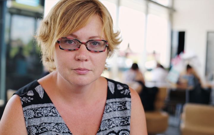 Eine Frau mittleren Alters, die in einem Büro sitzt. Sie sieht betrübt aus.