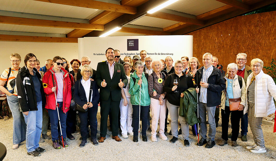 In einem großen Raum stehen vor einer Werbewand der Oper Burg Gars knapp 30 Personen für ein Gruppenfoto beisammen.