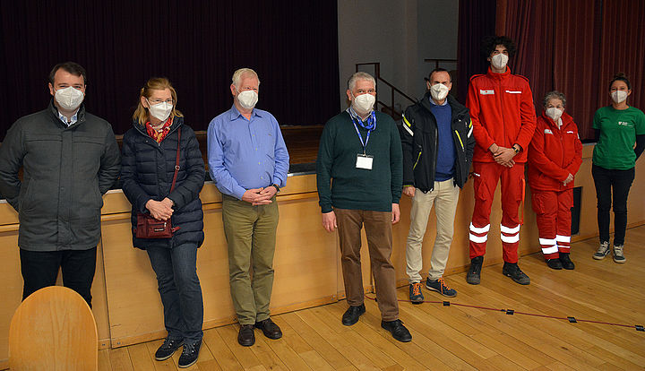 Acht Personen mit FFP2-Masken stehen im großen Saal vor der Bühne für ein Gruppenfoto mit Abstand.