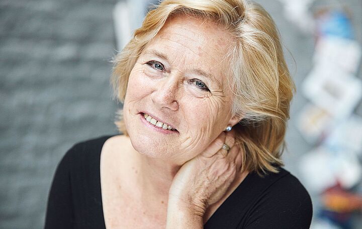 Eine etwas ältere Dame mit mittellangen, blond gefärbten Haaren, die etwas wehmütig in die Kamera schaut