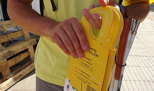 Der Blindenstock zusammengeklappt am Arm, in der Hand die Flyer: Es kann losgehen!