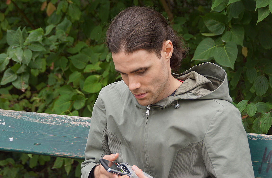 Ein junger Mann auf einer Parkbank mit einem Audio-Aufnahmegerät in den Händen.