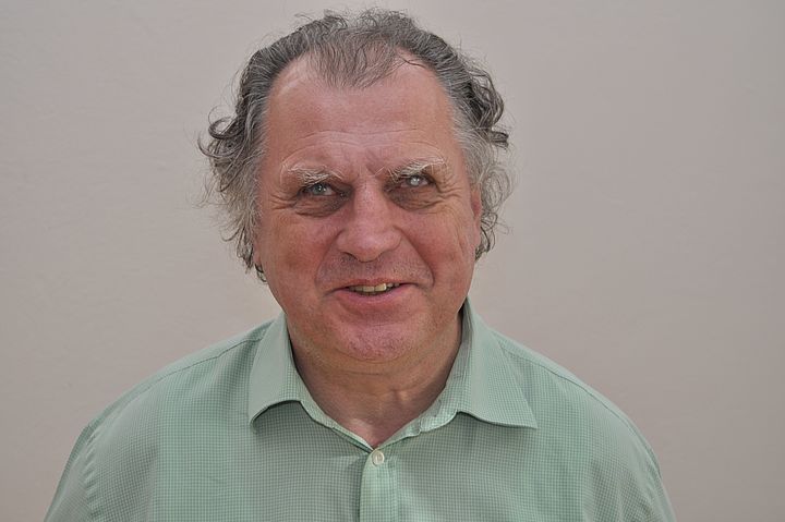 Portraitfoto, Prof. Erich Schmid in kariertem Hemd und mit grau melierten Haaren lächelt in die Kamera.