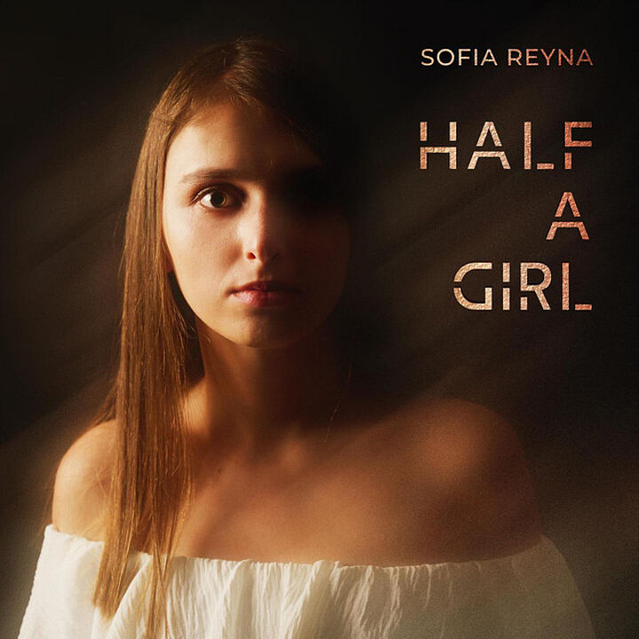 Das Gesicht einer jungen Frau mit glatten langen Haaren, nur rechtsseitig beleuchtet, die linke Gesichtshälfte ist im Dunklen. Text: Sofia Reyna HALF A GIRL