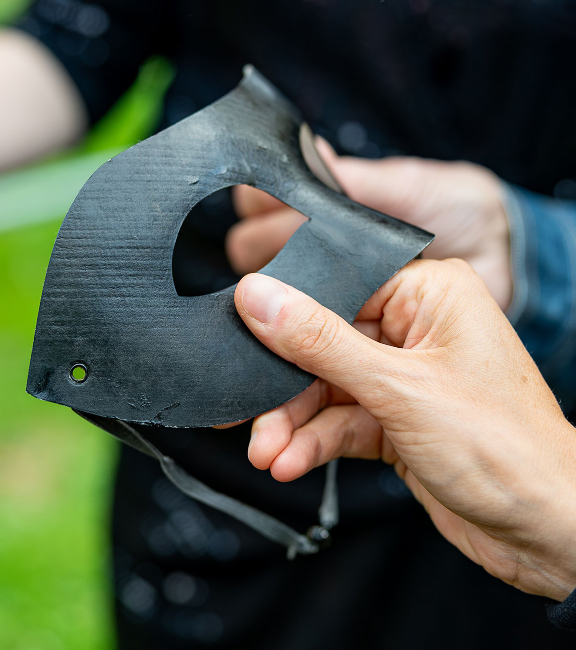 Zwei Hände halten eine feste Maske, die für die Bedeckung der Nase und den Bereich rund um die Augen des Trägers geformt ist.