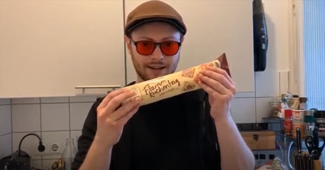 David zeigt eine Packung Flammkuchenteig in seiner Küche in die Webcam.