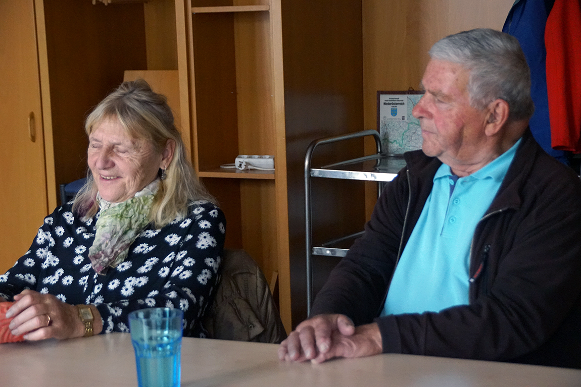 Eine Frau und ein Mann lachend nebeneinander an einem Tisch.