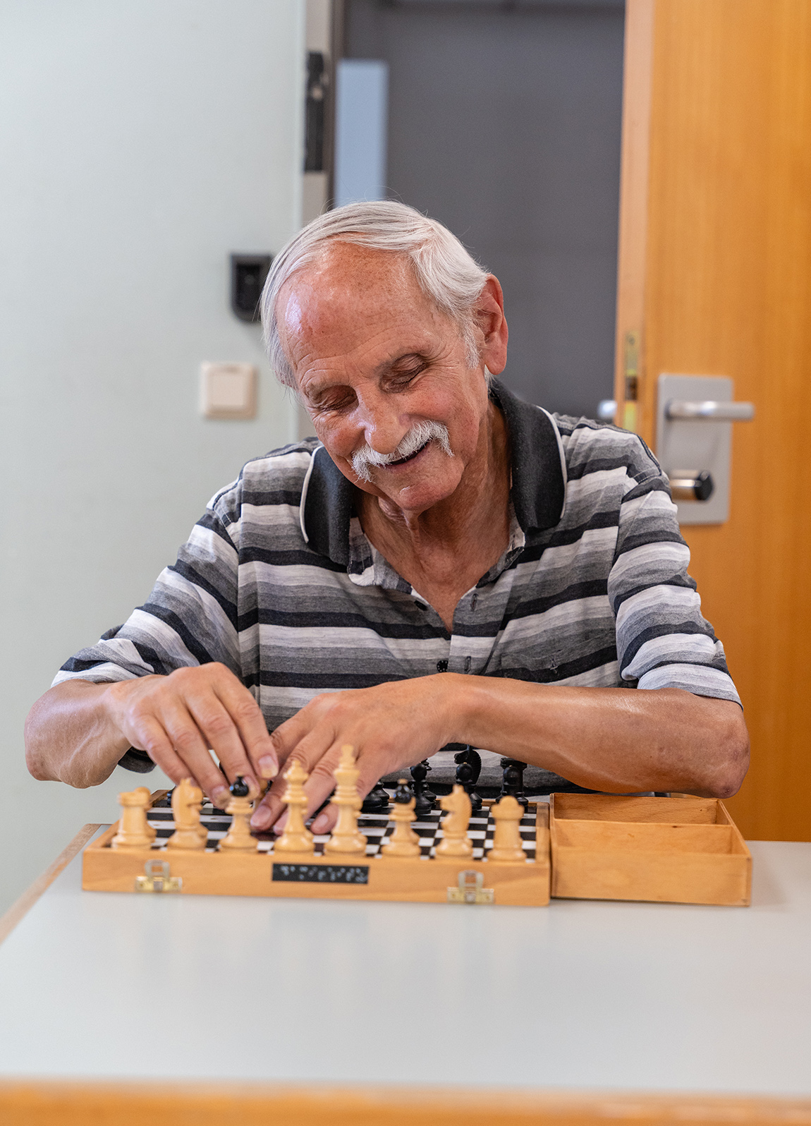 Ein lächelnder älterer Mann ertastet die Figuren auf einem Schachbrett für blinde Menschen.