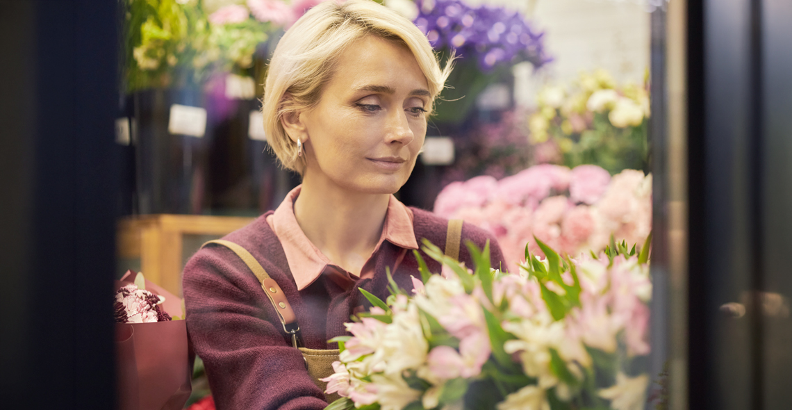 Eine blonde Frau in einem Blumengeschäft. Sie sieht traurig aus.